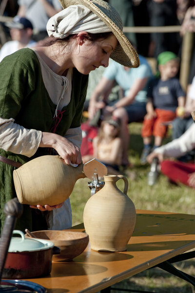Eine mittelalterlich gekleidete Frau schenkt Wasser in einen Tonkrug.