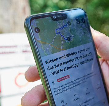 Eine Handy wird von zwei Händen gehalten. Auf dem Display ist ein Wandertipp zu sehen.