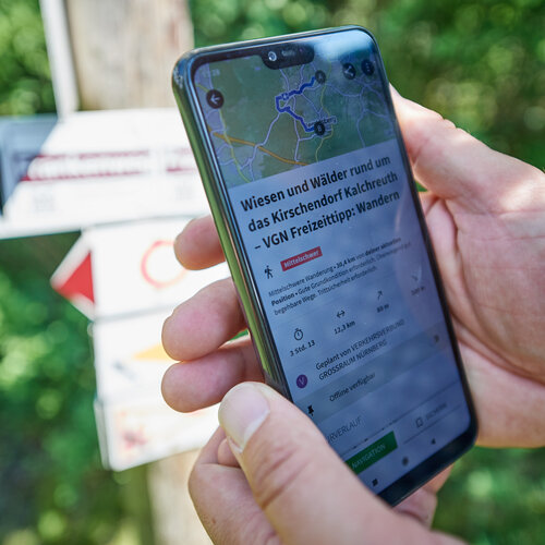 Eine Handy wird von zwei Händen gehalten. Auf dem Display ist ein Wandertipp zu sehen.