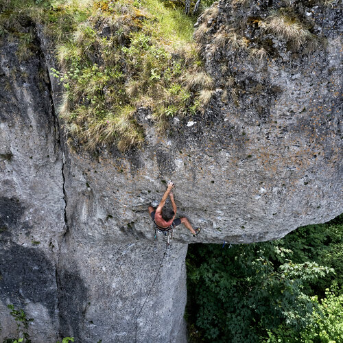 Ein Sportler mit freiem Oberkörber klettert an einem grauen Felsblock.